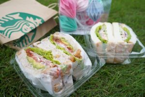 A person assembling sandwiches and organizing them into lunch containers on a kitchen counter.