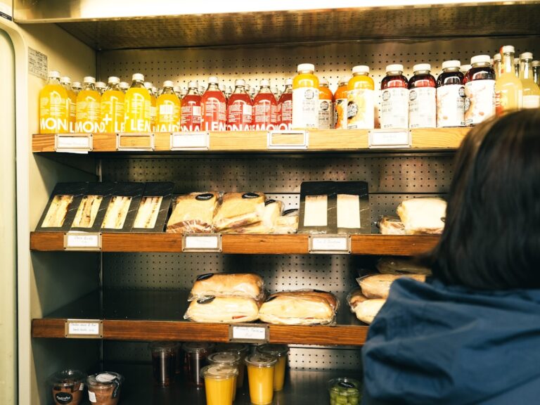 A person assembling a sandwich with fresh ingredients on a wooden kitchen counter.