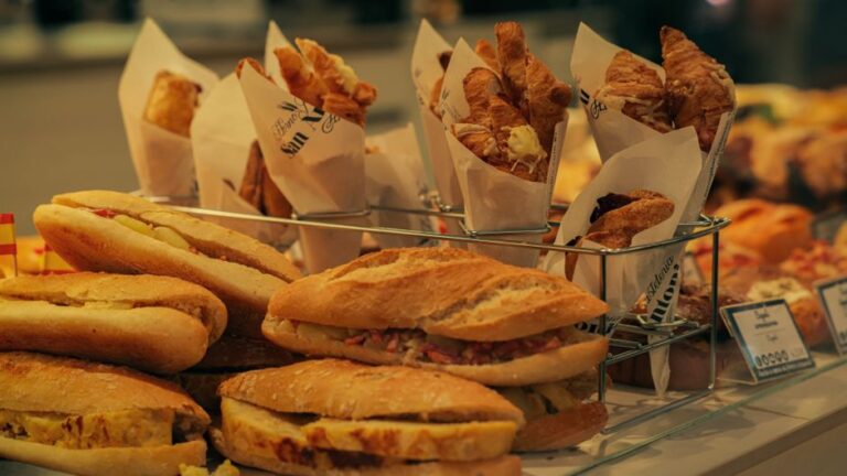 A close-up of assorted sandwiches wrapped in parchment paper, packed neatly in a picnic basket with an ice pack.