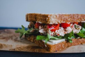 A person assembling a sandwich with whole grain bread, lean turkey, fresh greens, and sliced tomatoes on a kitchen counter.