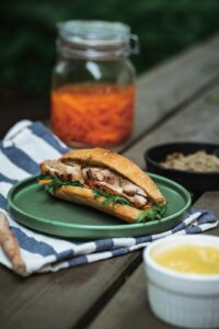 A person pairs a fresh sandwich with iced tea and sparkling water at an outdoor table.